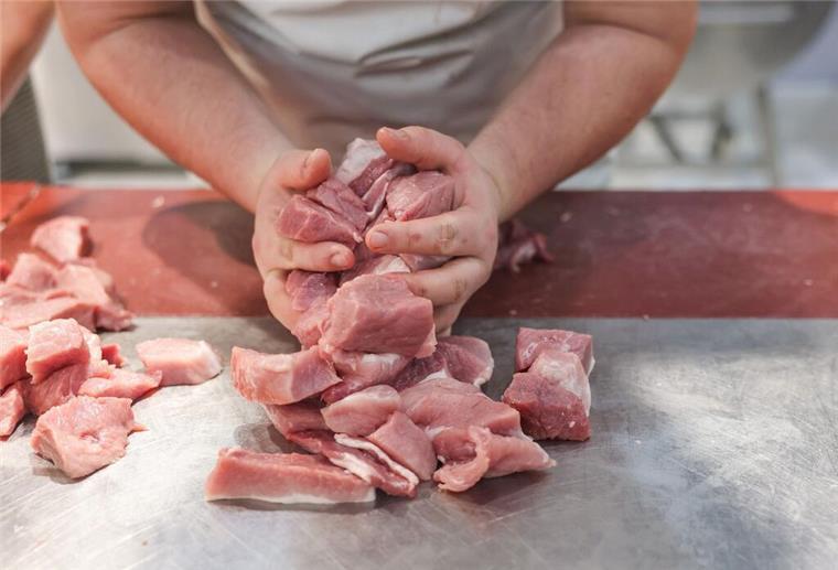 Erstes Kind gestorben - Behörden schließen Metzgereien Ein junger Metzger hält geschnittenes Schweinefleisch in der Hand.