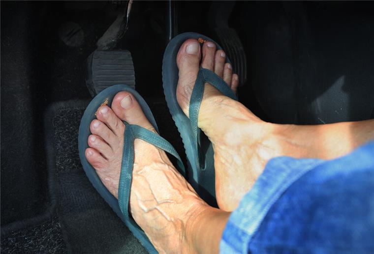 Mit Flip-Flops oder barfuß Autofahren: Was erlaubt ist – und wann es teuer wird Ein Mann trägt Flip-Flops und fährt Auto.