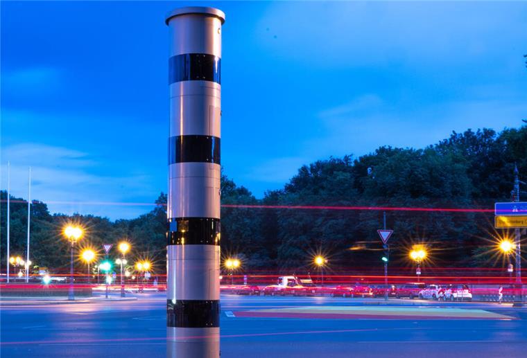 Eine Blitzsäule steht am Kreisverkehr an der Siegessäule, während im Hintergrund vorbeifahrende Fahrzeuge Lichtspuren hinterlassen (Aufnahme mit Langzeitbelichtung).