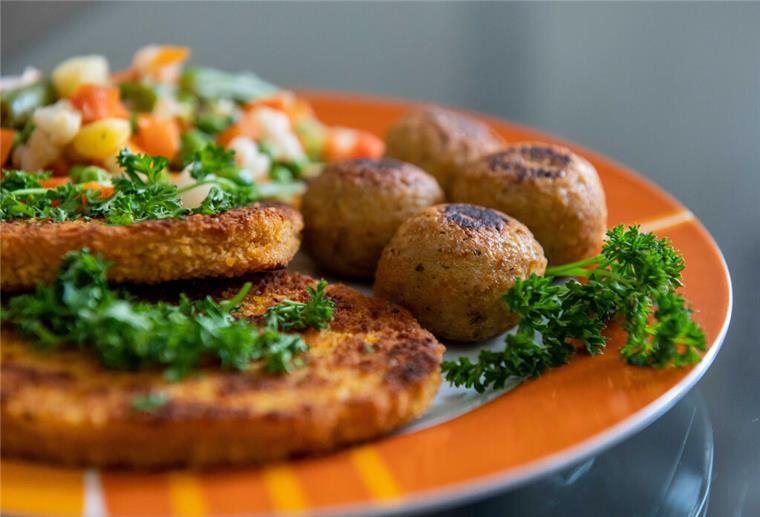 Fleischersatz im Check: Wie gesund sind vegane Produkte wirklich? Falafel, vegane Schnitzel und Gemüse liegen auf einem Teller in einer Küche.