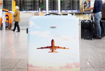 Ein Koffer mit einem aufgedruckten Flugzeug steht in der Abflughalle eines Flughafens.