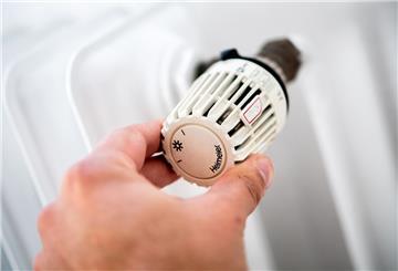 Ein Mann dreht in einer Wohnung am Thermostat einer Heizung
