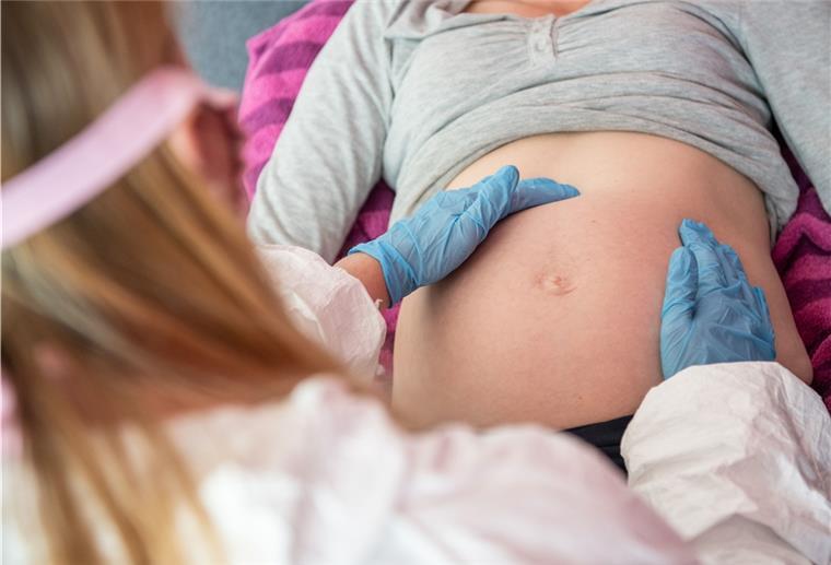 Eine Hebamme tastet den Bauch einer schwangeren Frau ab.