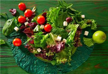 Ein grüner Salat mit Tomaten und Feta auf einem Teller. Obst und Gemüse sind gute Quellen für natürliche Vitamine, die der Körper jeden Tag braucht.