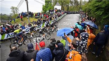 Olympiasieger Remco Evenepoel (M) mit goldenem Helm an der Mauer von Huy. Rechts neben ihm Tadej Pogacar.