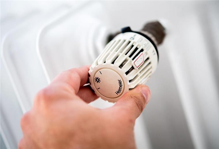 Ein Mann dreht in einer Wohnung am Thermostat einer Heizung.