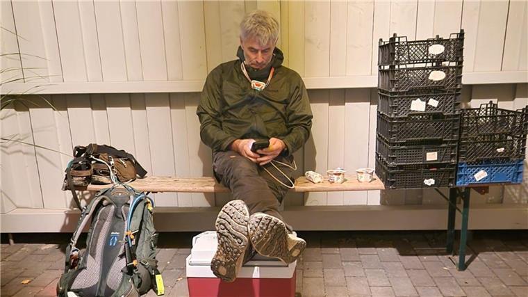 Ein Mann sitzt auf einer Bank neben einem Rucksack und Körben.