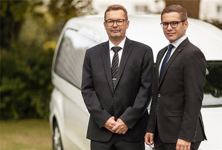 Hadeler-Bestattungen feiert 150. Jubiläum Zwei Männer in schwarzen Anzügen vor weißem Bestattungswagen