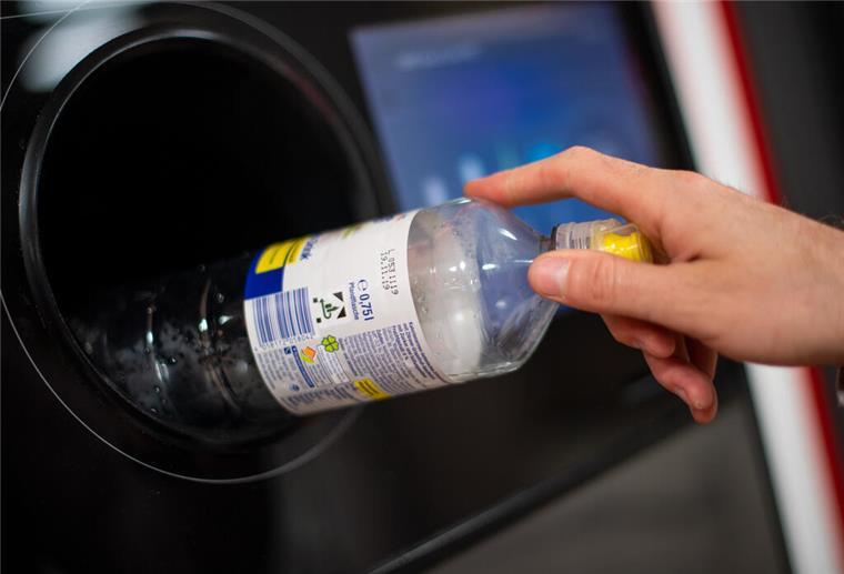 Ein Mann steckt eine Pfandflasche in einen Pfandflaschenautomaten in einem Supermarkt