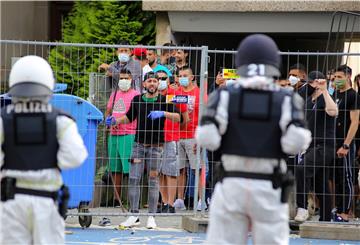 Polizisten sehen sich einer Gruppe junger Männer gegenüber, die sich hinter einem Zaun versammelt hat.
