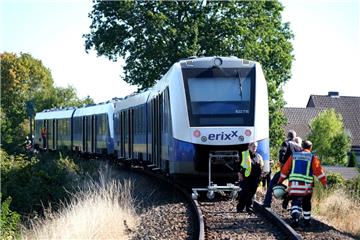 Polizisten und Rettungskräfte der Feuerwehr stehen vor einem verunglückten Zug auf dem Bahngleis bei Isenbüttel.


