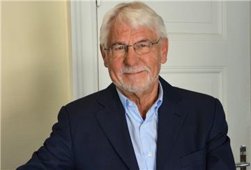 Ein älterer, gepflegter Mann im Anzug lächelt in die Kamera.