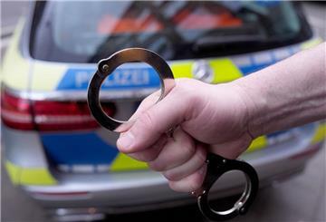 Ein Polizist hält Handschellen vor einem Einsatzfahrzeug hoch.