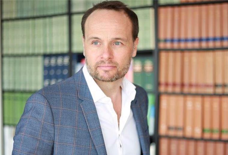 Rechtsanwalt Wolfgang Wittmann steht vor einem Bücherregal.