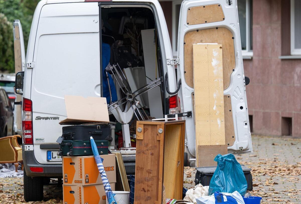 Möbel und Umzugskartons stehen vor einem Transporter an einem Wohnhaus.
