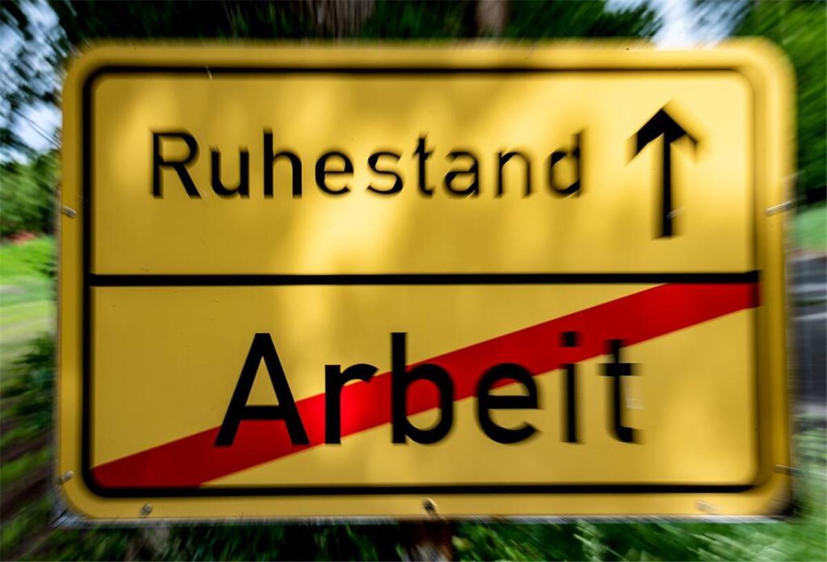 Ein Schild steht am Straßenrand in der Optik eines Ortsschildes, auf dem das Wort "Arbeit" durchgestrichen und der Weg Richtung "Ruhestand" ausgeschildert ist.
