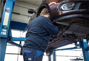 Ein Mechaniker schaut in einer Kfz-Werkstatt in den Radkasten eines Autos. 