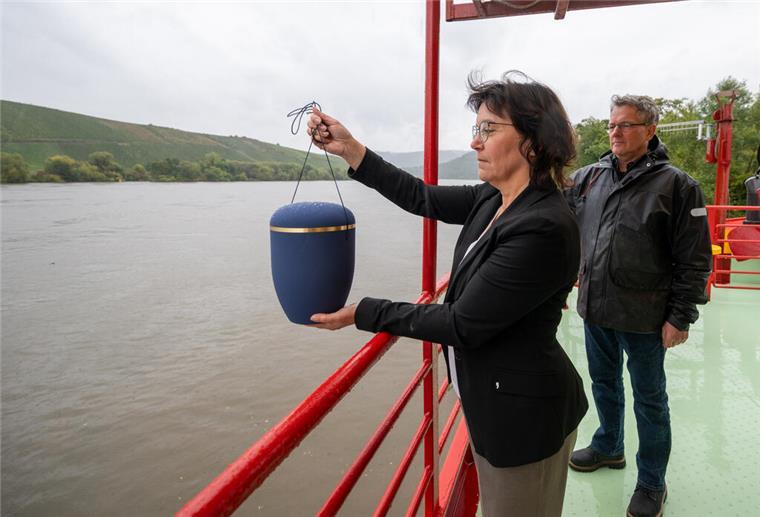 Eine Frau steht an der Rehling eines Schiffes und hält eine Urne in der Hand.