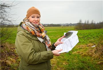 Frau mit Brief in der Hand steht in der freien Landschaft auf der grünen Wiese.