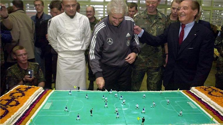 Rote Karten, Bundeswehr: Was Völler 2002 in Bosnien erlebte Rudi Völler (M) schneidet beim Truppenbesuch in Sarajevo eine Torte in Form eines Fußallplatzes an.