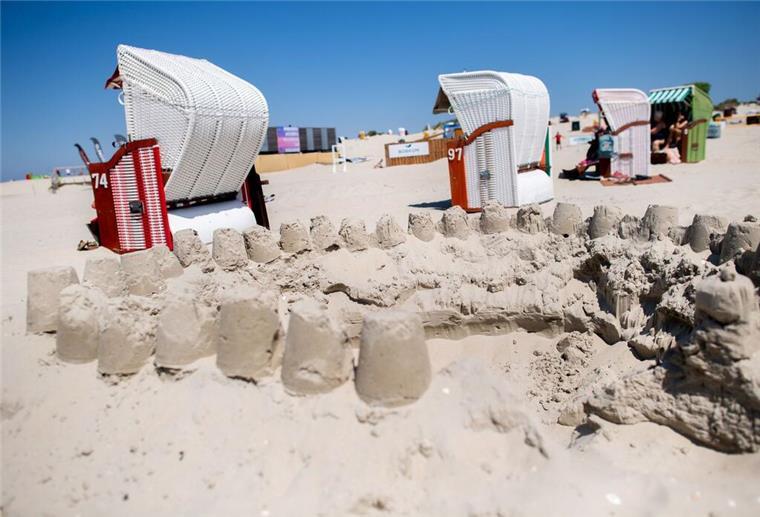 Zahlreiche Strandkörbe stehen bei sonnigem Wetter hinter einer Sandburg am Strand der Insel Borkum.
