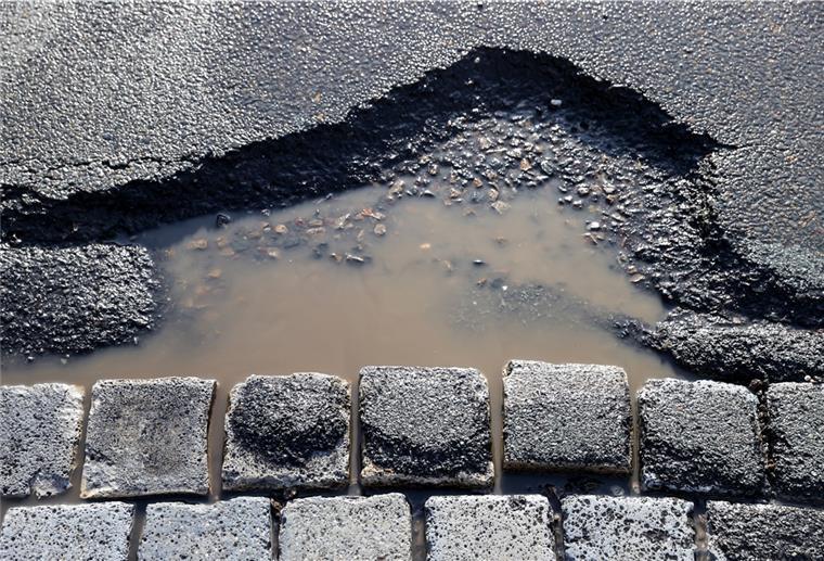 Hier kannst du kaputte Straßenlaternen von der Couch aus melden Neben losem Kopfsteinpflaster sammelt sich Regen in einem Schlagloch.
