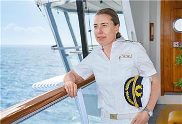eine Frau in Kapitänsuniform steht an der Reling eines Schiffes