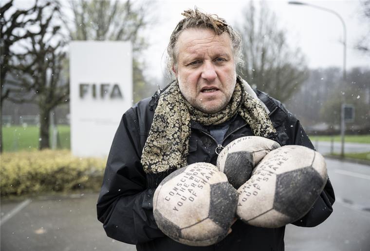 Künstler aus Osnabrück protestiert gegen WM in Katar Ein Mann steht mit drei Fußbällen in der Hand vor einem Schild mit der Aufschrift FIFA.