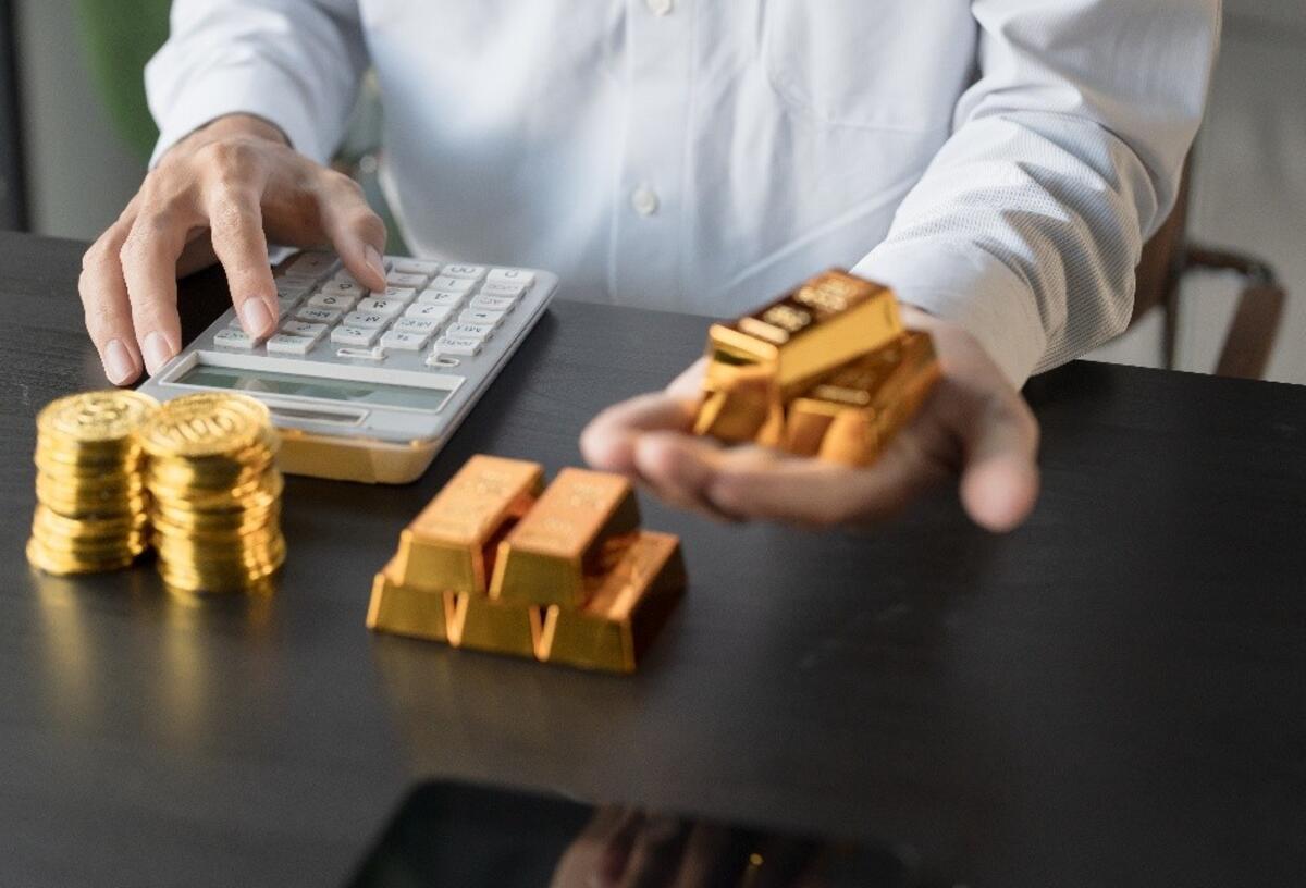Gold oder Immobilien? Welche Anlageform passt zu wem? Person mit Taschenrechner und Gold