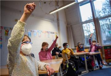 Eine Schülerin einer 4. Klasse hebt im Unterricht mit Maske die Hand. 