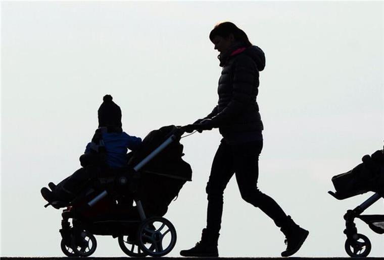 Eine Mutter schiebt ihren Kinderwagen eine Landstraße entlang.