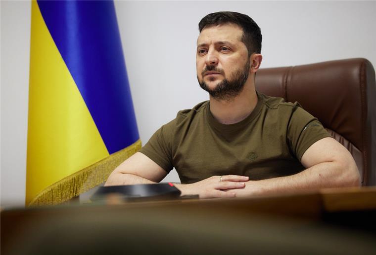 Wolodymyr Selenskyj, Präsident der Ukraine bei einer Konferenz. Im Hintergrund die Ukraine Flagge.
