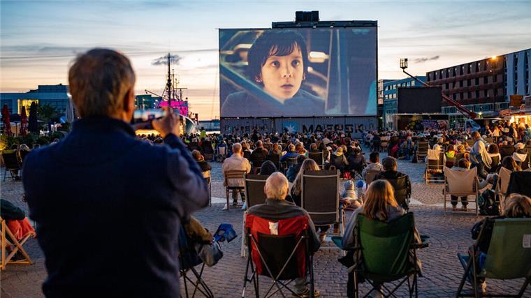 Bremerhaven verliert beliebtes Kino im Hafen: So geht es jetzt weiter Im Fischereihafen ist eine riesige Leinwand aufgebaut, auf der ein Film zu sehen ist. Davor sitzen Hunderte Besucher.