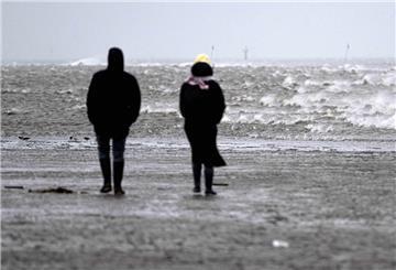 Spaziergänger gehen bei stürmischem Wetter durch das Watt vor dem Strand von Cuxhaven.