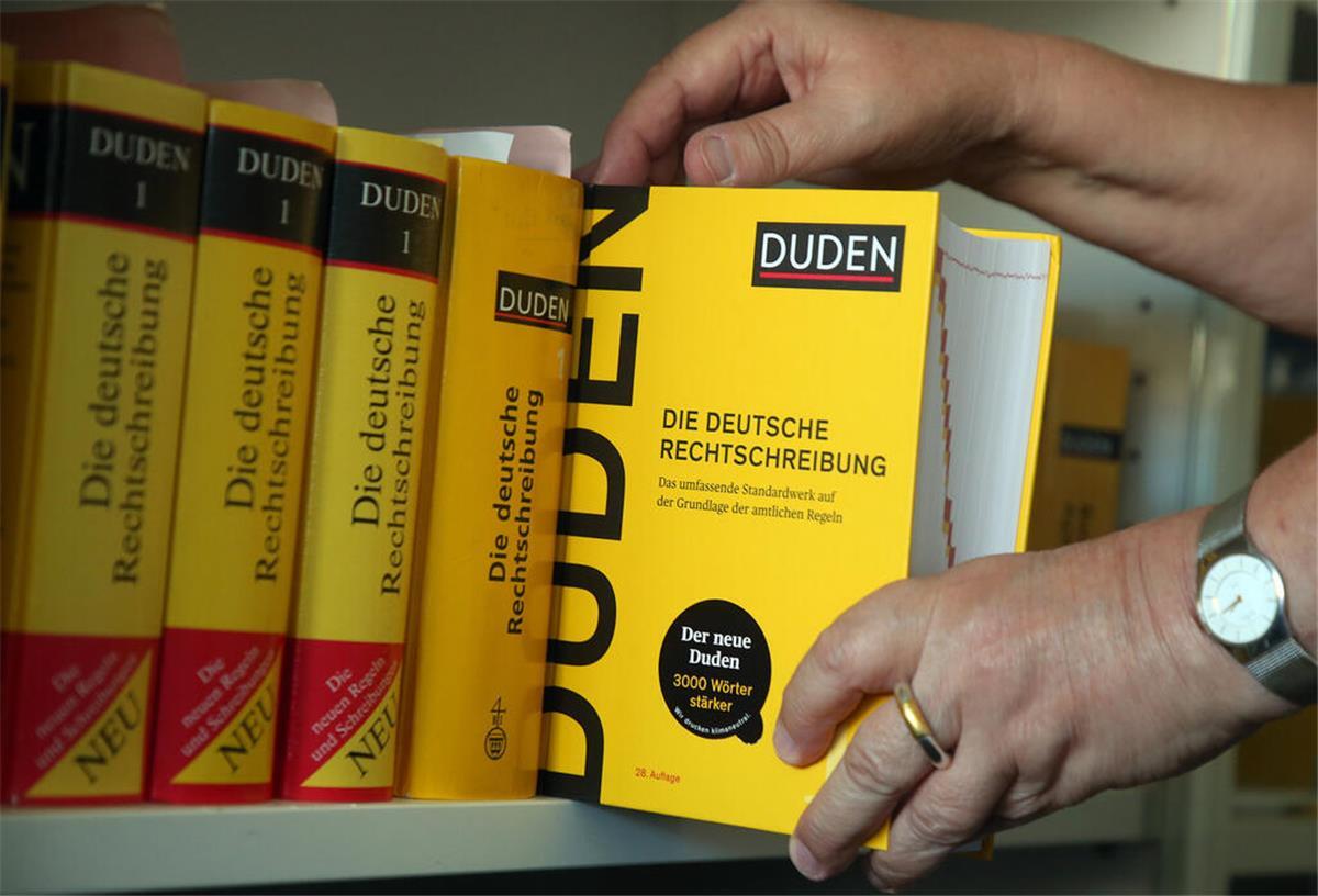 Von „Afterweisheit“ bis „verschimpfieren“ - Diese Wörter wurden aus dem Duden gestrichen Eine Person stellt einen Duden ins Bücherregal.
