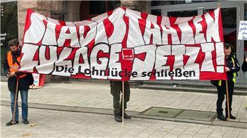 „Stadtstaaten - Zulage jetzt! - Die Lohnlücke schließen“ steht auf einem Plakat, das Demonstrierende vor dem Gewerkschaftshaus halten.