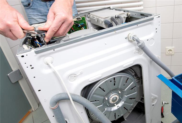 Wie ihr bei Haushaltsgeräte-Reparaturen bares Geld sparen könnt Ein Mann repariert eine Waschmaschine. Die Verbraucherzentrale warnt vor unseriösen Reparaturdiensten.