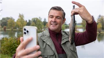 Stolz posiert Wirt Jo (Christian K. Schaeffer) für ein Selfie, das seinen erfolgreichen Fischfang dokumentieren soll.