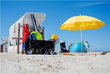 Ein Sonnenschirm steht bei sonnigem Wetter neben einem Strandkorb am Strand