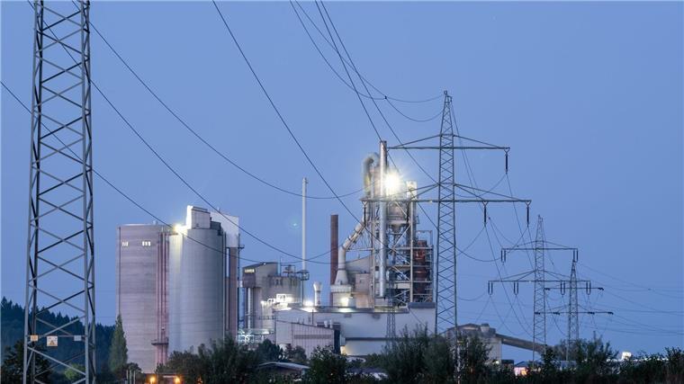 Kabinett will CO2-Speicherung in Deutschland möglich machen Strommasten stehen im Morgenlicht vor einem Zementwerk.