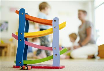 Symbolbild: Eine Erzieherin spielt in einer Kindertagesstätte hinter einer Rollbahn mit Kindern.