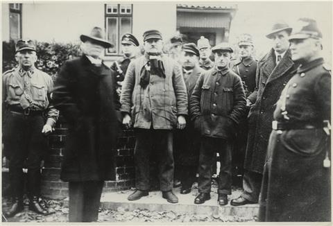 Täter und Opfer: Vor dem Haus von Erich Neugarten in der Zevener Gartenstraße haben der Führer des Zevener SA-Sturms Wilhelm Schnase (links) und seine Männer unter den Augen eines Polizisten (rechts) und seiner Kollegen Erich Neugarten (Zweiter von rechts), Hermann Samson (Vierter von rechts), Bernhard Blumert (Sechster von rechts), vermutlich Kurt Deichmann (hinter Blumert), Albert Rosenthal (Vierter von links) und vermutlich Gustav Kleinschmidt (Zweiter von links) vor dem Abtransport zur Gesta