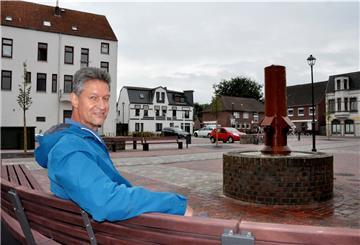 Tim Lorenz hat Platz genommen auf einer Bank auf dem von ihm gestalteten Blexer Dorfplatz. Die Gestaltung des Platzes ist abgeschlossen. Das Gesamtensemble wird fertig sein, wenn die GNSG die beiden geplanten Miethäuser errichtet hat.