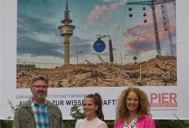 Wasserstoff: Großes Plakat an der Kennedybrücke Torsten Tingler freut sich zusammen mit Katharina Perokovic und Nicole Halves-Volmer von der Erlebnis Bremerhaven GmbH über das Großflächenplakat seines Gewinnerbildes an dem Standort Columbusstraße, Höhe Hochschule Haus C.