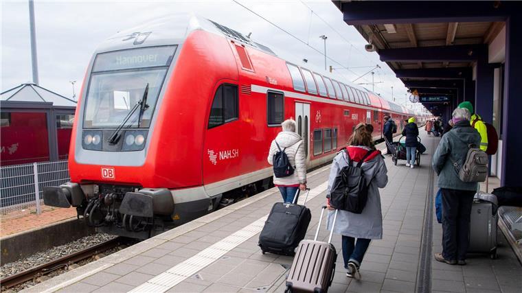 Touristen laufen mit Rollkoffern am Bahnhof Norddeich-Mole entlang.