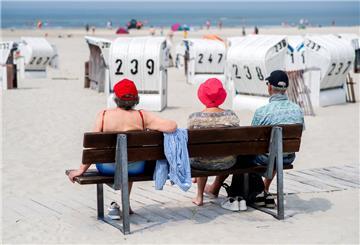 Drei Touristen sitzen bei sonnigem Wetter auf einer Bank an einem Strand .