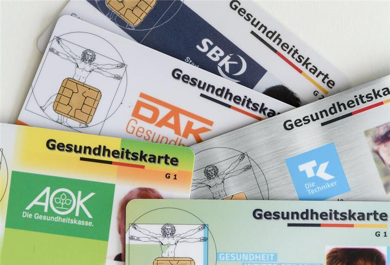 Gesundheitskosten explodieren: Krankenkassen melden neuen Rekordwert! Gesundheitskarten verschiedener Krankenkassen liegen auf einem Tisch.