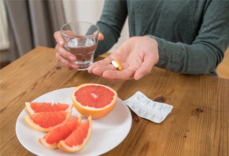 Grapefruit verträgt sich nicht mit allen Medikamenten Eine Frau hat Medikamente und ein Glas Wasser in den Händen. Vor ihr steht ein Teller mit Grapefruit.