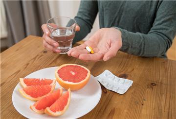 Eine Frau hat Medikamente und ein Glas Wasser in den Händen. Vor ihr steht ein Teller mit Grapefruit.