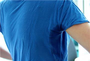 Eine Person zeigt ihren Schweiß-Fleck am T-Shirt. 